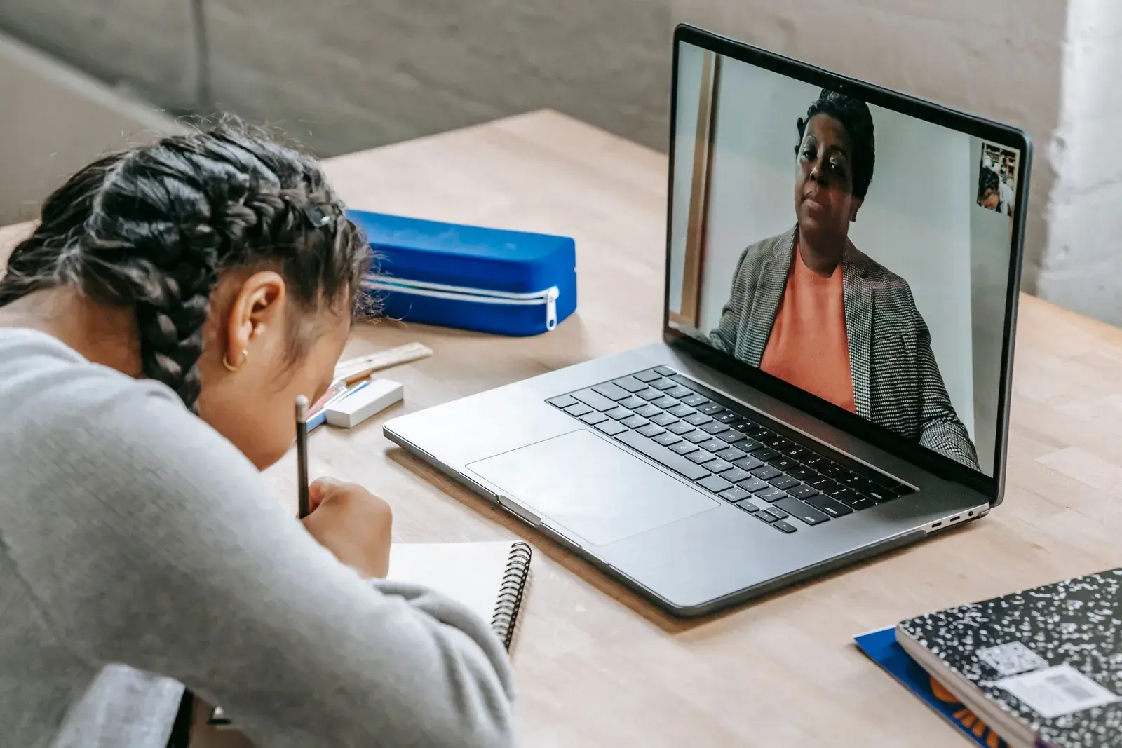 Học sinh vừa ghi chép vừa học trực tuyến với giáo viên hiện trên màn hình laptop