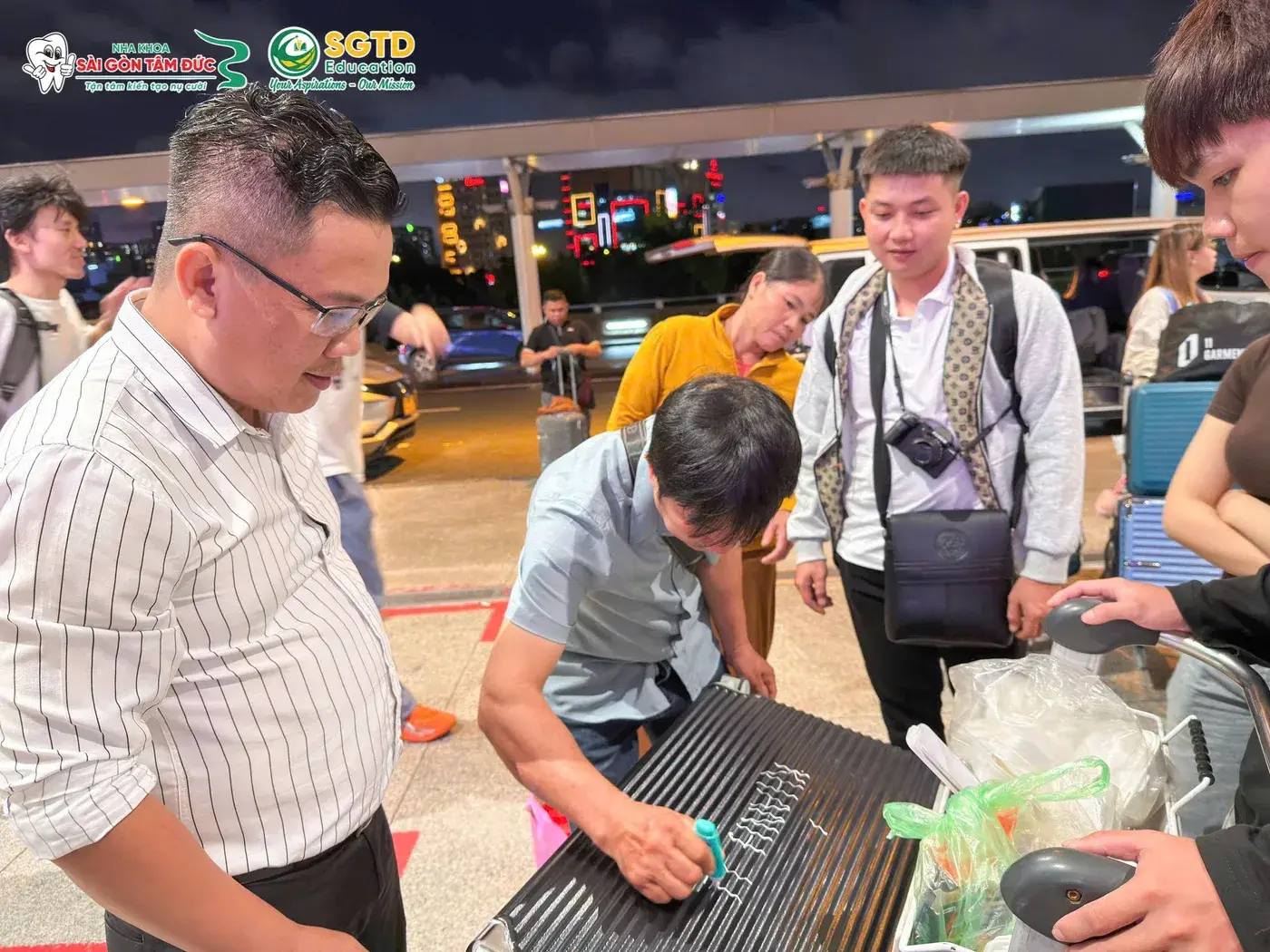 Người thân ghi tên Giang Khánh lên vali bên ngoài nhà ga, đại diện SGTD Education đứng cạnh