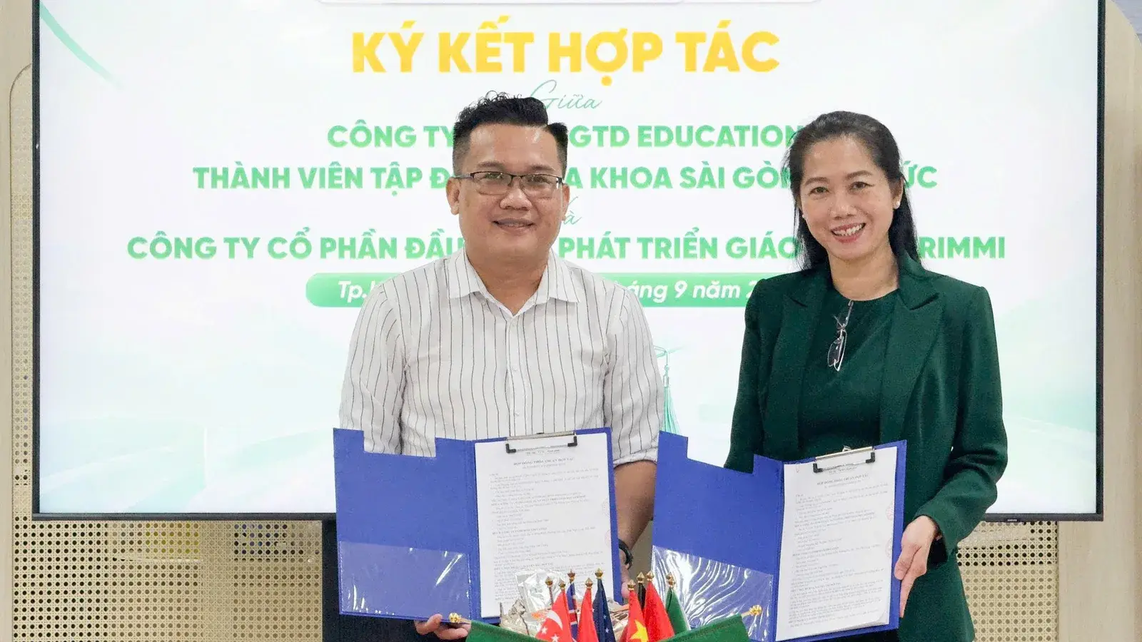 Đại diện SGTD Education và Gerimmi cầm văn bản thỏa thuận hợp tác vừa ký trước màn hình lễ ký kết