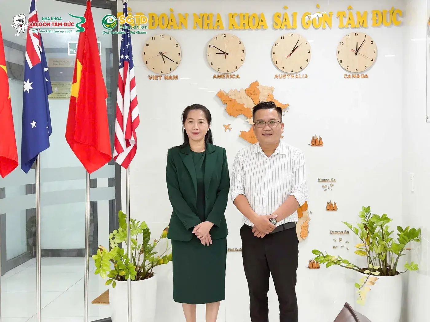 Hai đại diện ký kết chụp ảnh lưu niệm bên bức tường đồng hồ bốn múi giờ