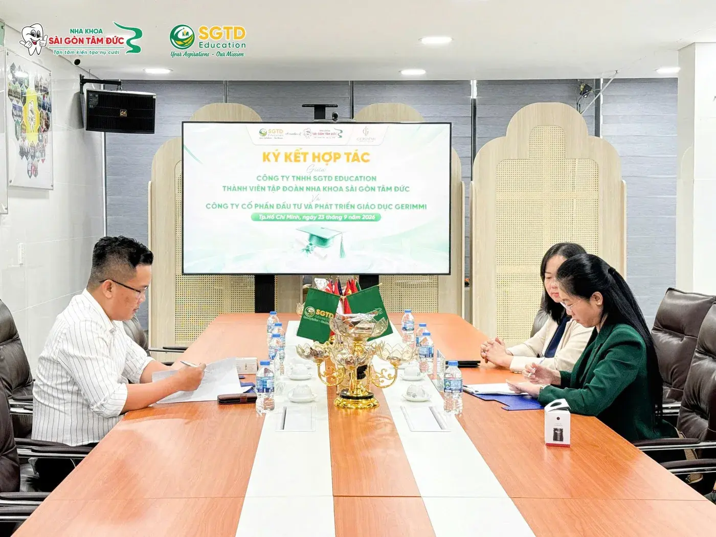 Đại diện SGTD Education và Gerimmi ký văn bản hợp tác dưới màn hình lễ ký kết ngày 23/09/2026