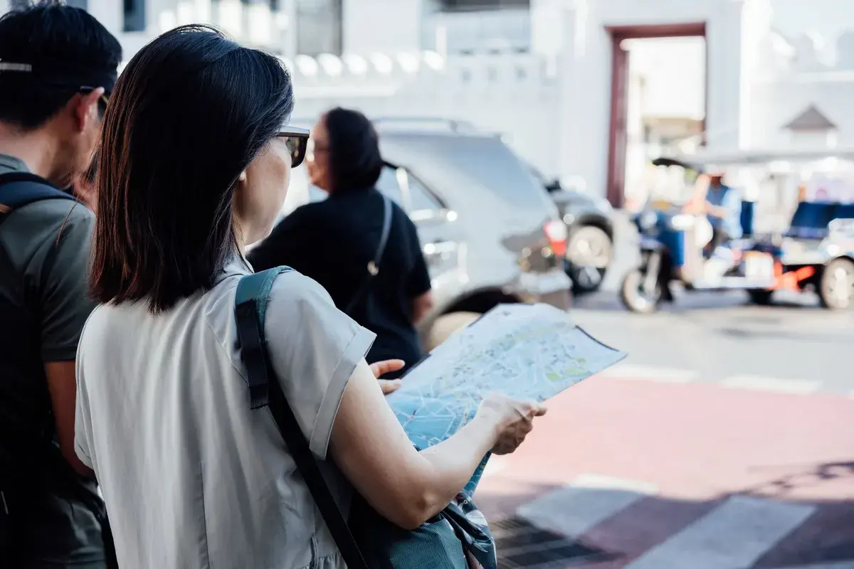 Một nữ du khách đứng bên đường, mở tấm bản đồ giấy và chỉ vào lộ trình
