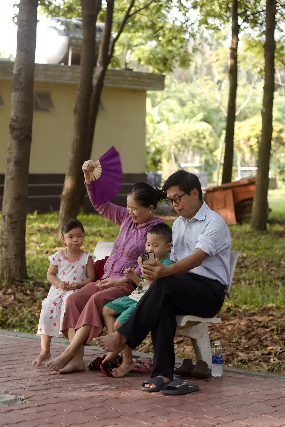 Ông bà cùng hai cháu nhỏ ngồi chơi trên ghế đá công viên tại Việt Nam